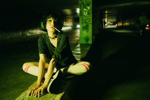 Free A young woman sits in a gritty urban environment at night, with edgy street fashion. Stock Photo