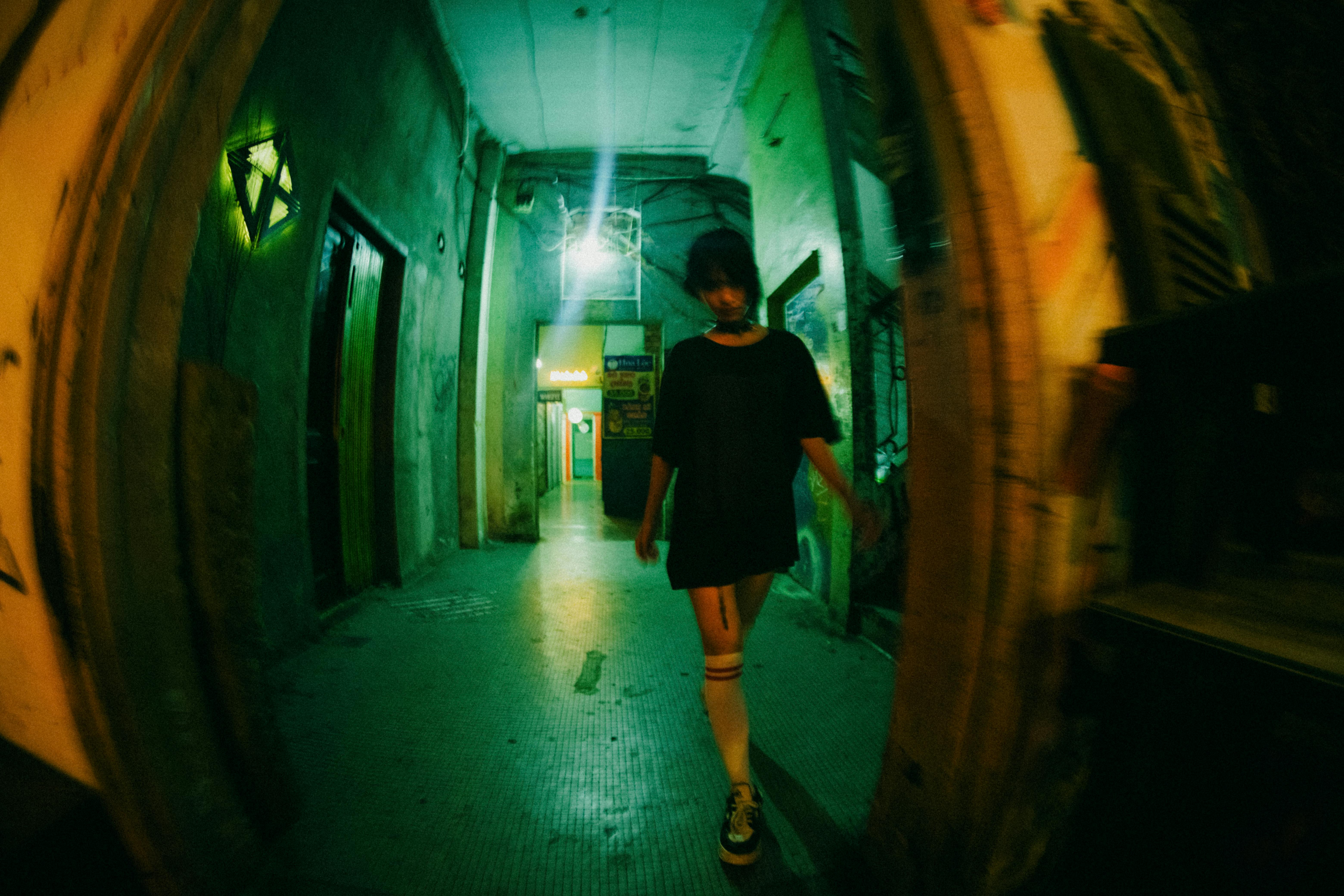 A young woman walks through an illuminated corridor at night, captured with a fisheye lens.