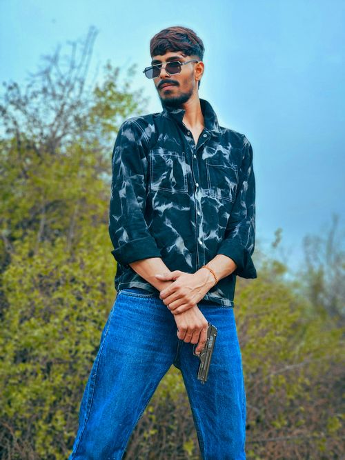 Free Young man with sunglasses and a gun posing confidently against a natural background. Stock Photo