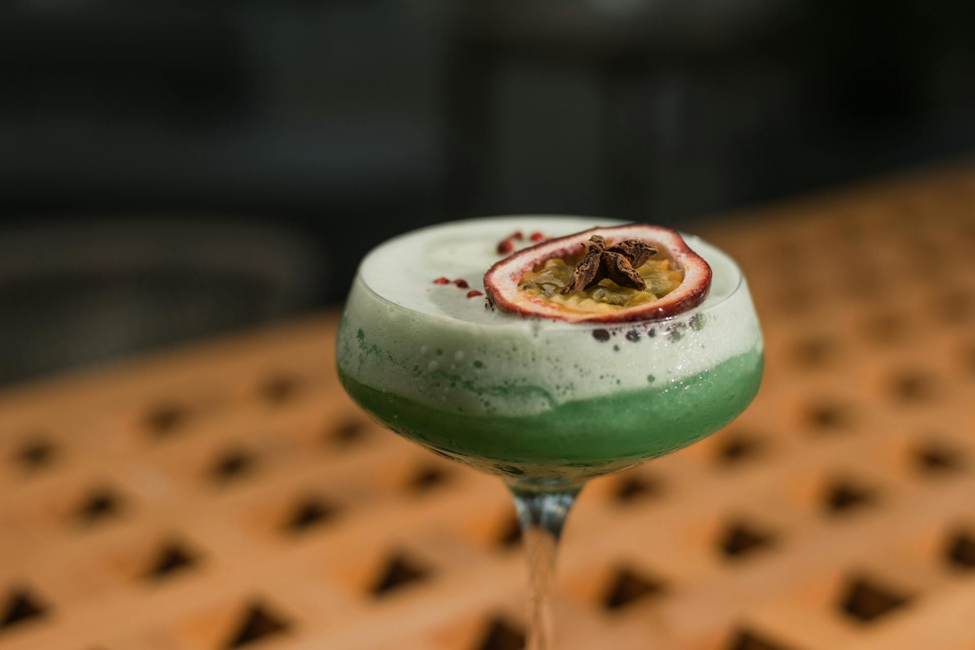 Close-up of a vibrant green cocktail topped with foam and a passion fruit garnish.