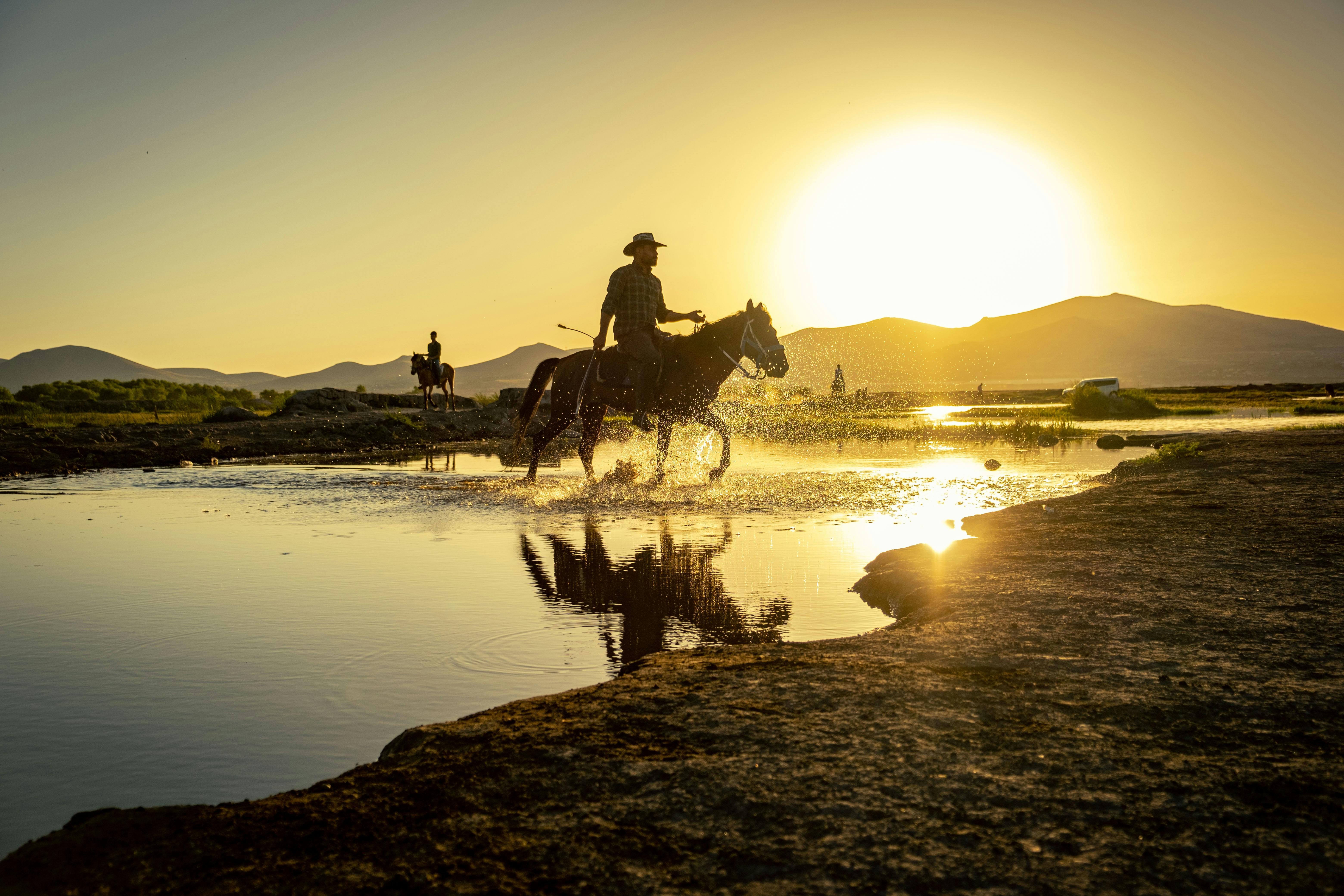 cowboy crossing river on horse at sunset