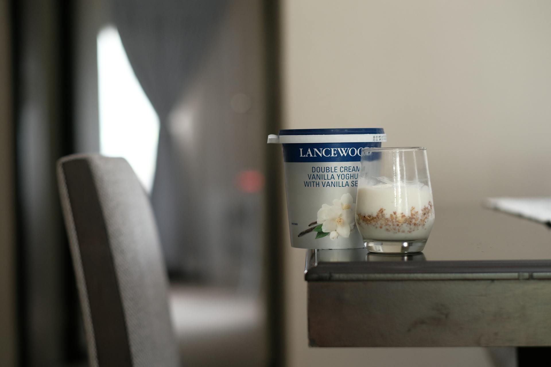 Vanilla yogurt container with a glass on a modern indoor table setting.