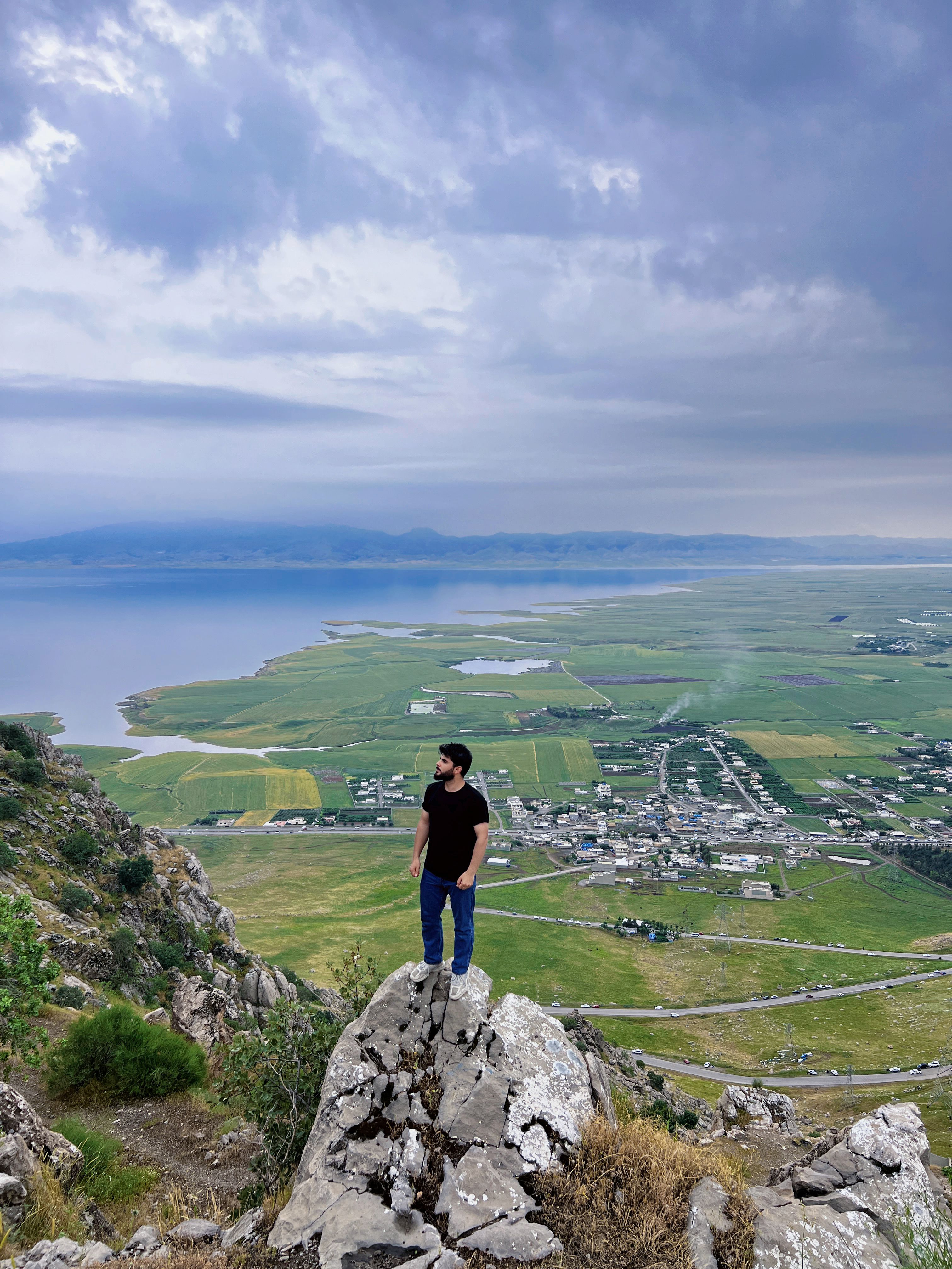 A man stands on a rocky cliff, overlooking the scenic landscape of Qurago in Sulaymaniyah, Iraq.