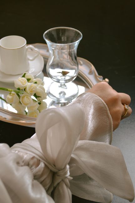 Elegant bridal setup with glass, cup, and roses on a reflective tray, showcasing timeless wedding charm.