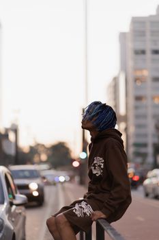 Stylish model with blue hair sitting on a railing in an urban street setting.