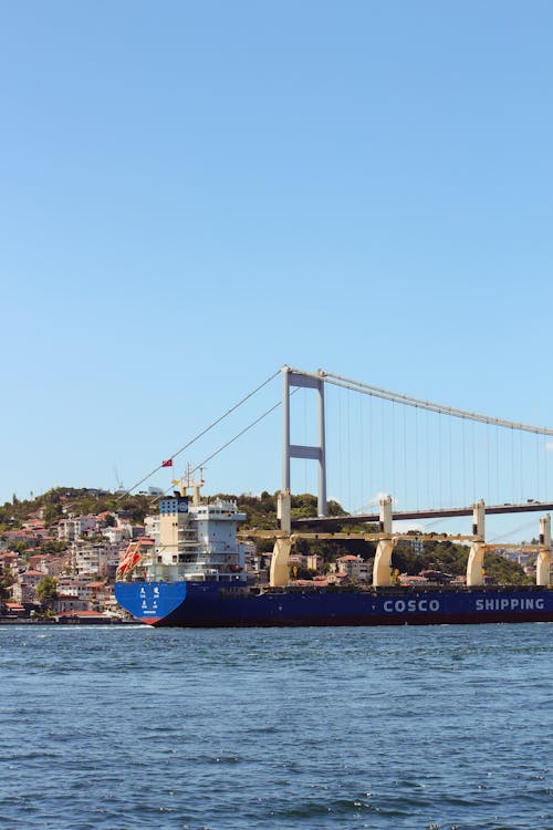 A large ship is traveling under a bridge