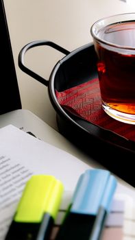 A cup of tea on a tray beside highlighters and paper, captured in a minimalist style.