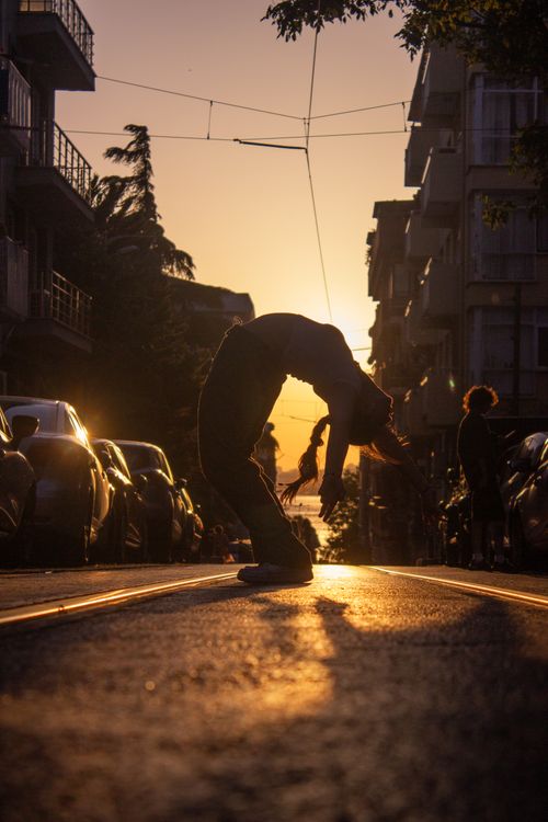 Free A dancer performing a dramatic silhouette pose on a city street during sunset, capturing the urban vibe. Stock Photo