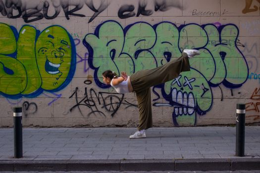 Woman performing a gymnastics pose in front of a vibrant graffiti wall on an urban sidewalk.