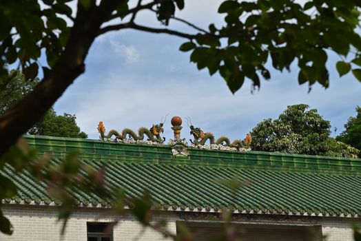Intricate dragon statues atop a traditional temple roof surrounded by trees.