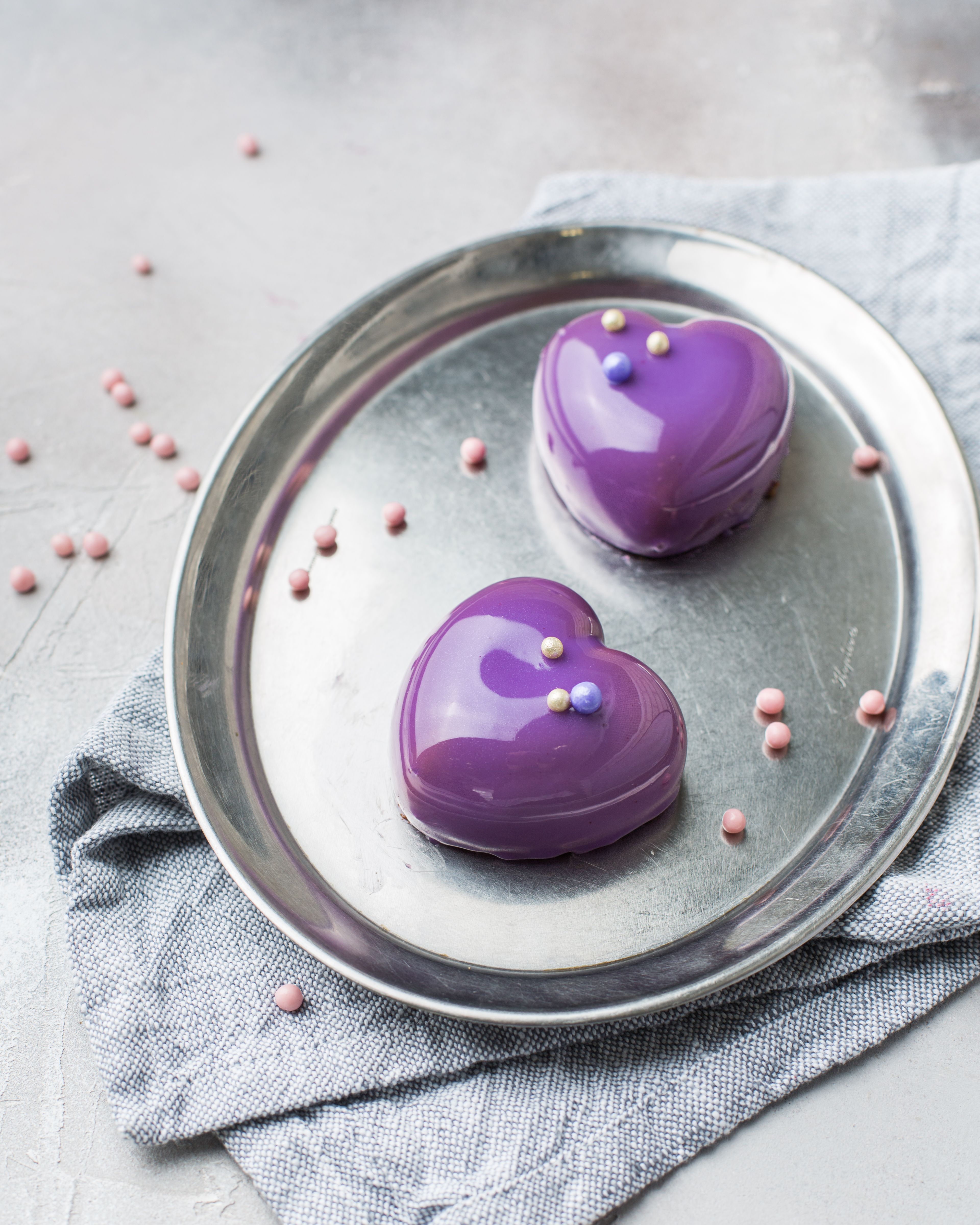 Charming purple heart-shaped desserts with glossy icing on a metal tray, perfect for romantic occasions.