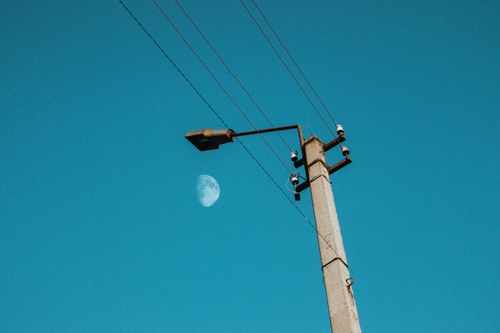 Free Streetlight with power lines under a clear blue sky and visible moon. Stock Photo