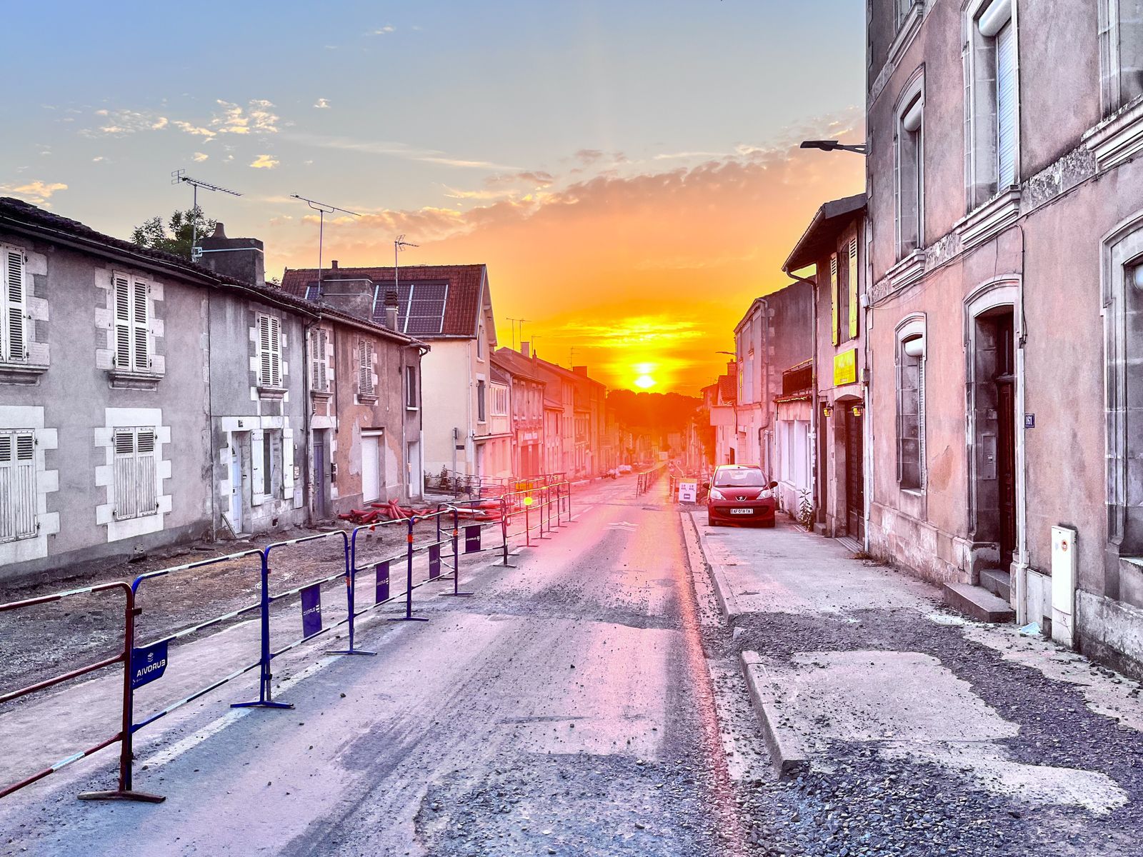 Coucher de soleil sur une rue en travaux bordée de vieilles maisons en pierre