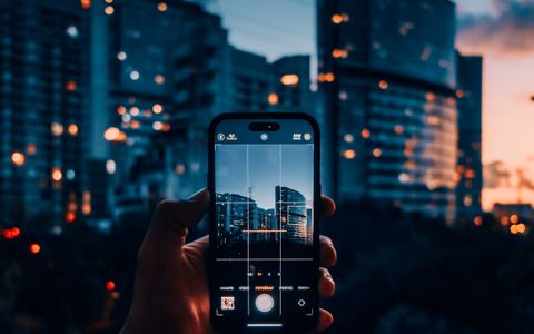 Mano fotografiando rascacielos con el móvil al atardecer
