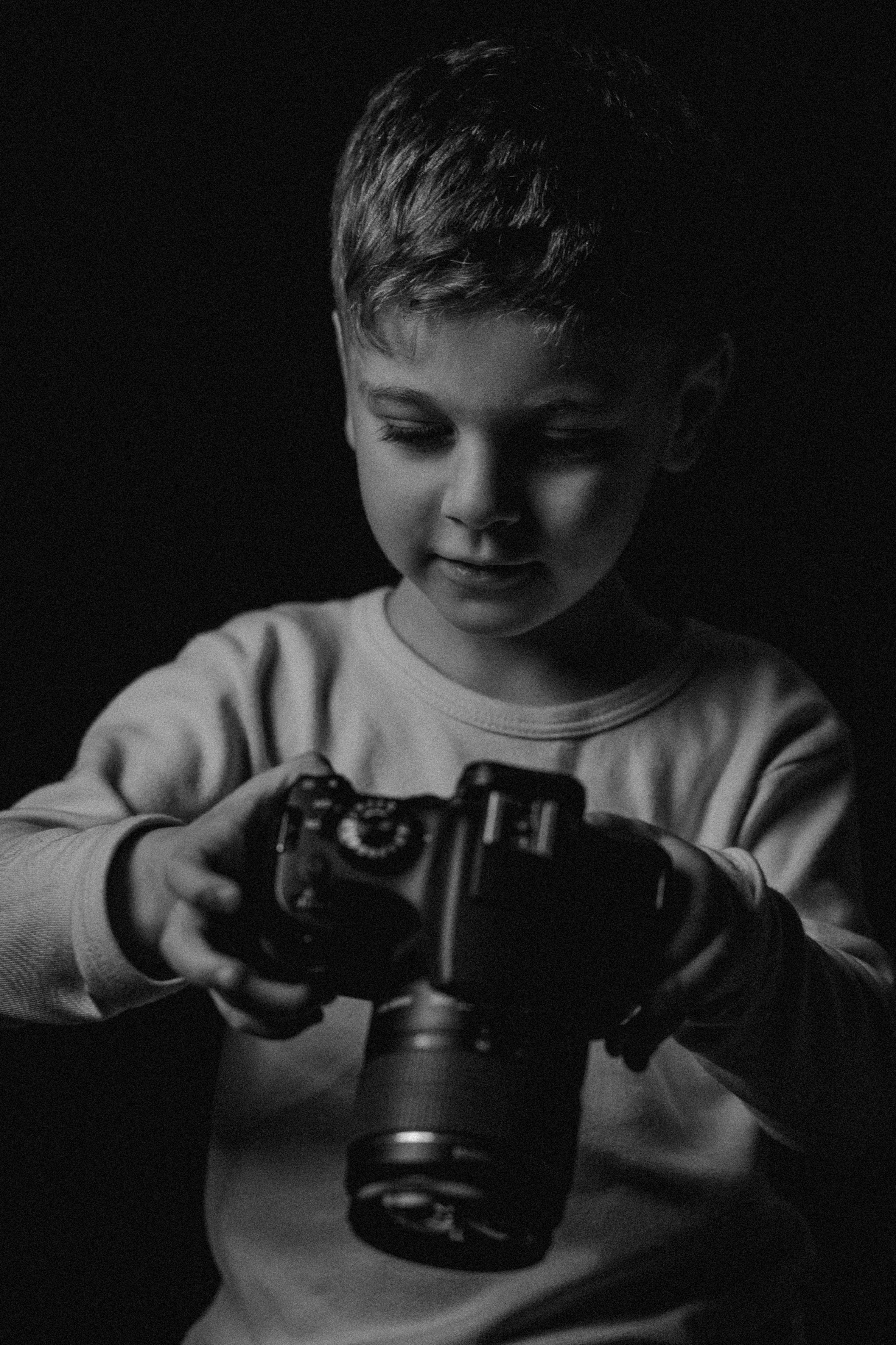 A young boy curiously operating a DSLR camera in a black and white portrait.