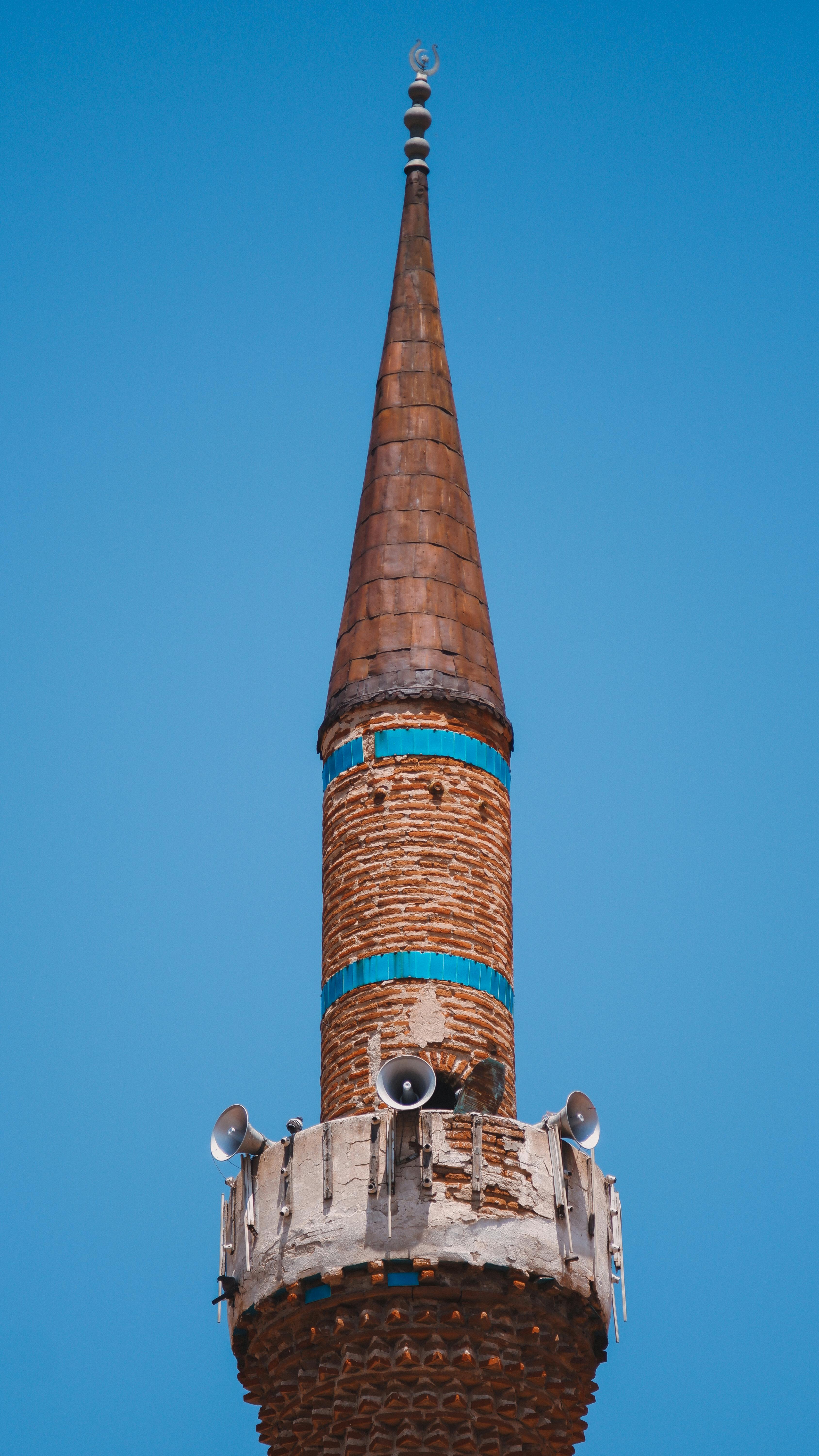A brown brick minaret adorned with speakers against a clear blue sky.