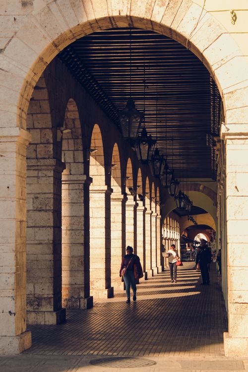 Free A scenic colonnade in a city with warm lighting and people walking along it. Stock Photo
