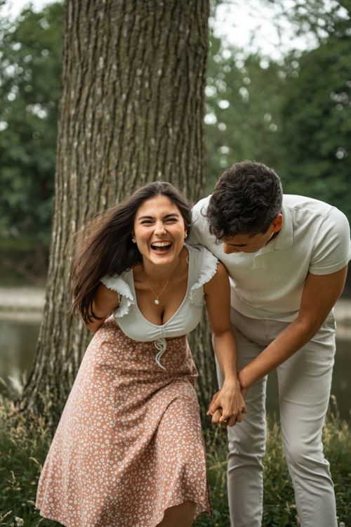 Free A happy couple shares a laugh by a tree in a tranquil outdoor setting. Perfect for lifestyle themes. Stock Photo