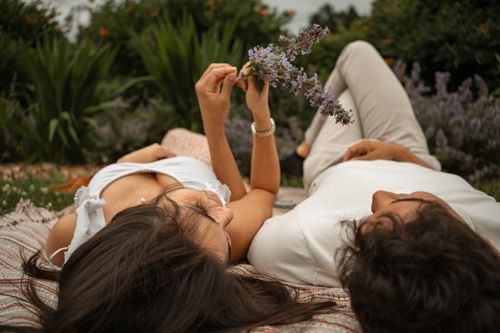 Free A couple lying on a blanket in a garden, holding a flower, enjoying a peaceful moment together. Stock Photo