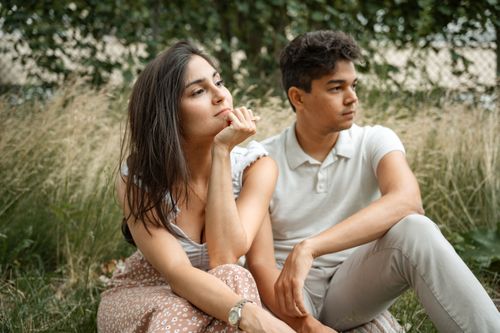 Free A thoughtful couple sitting together in a tranquil grassy field, enjoying the outdoors. Stock Photo
