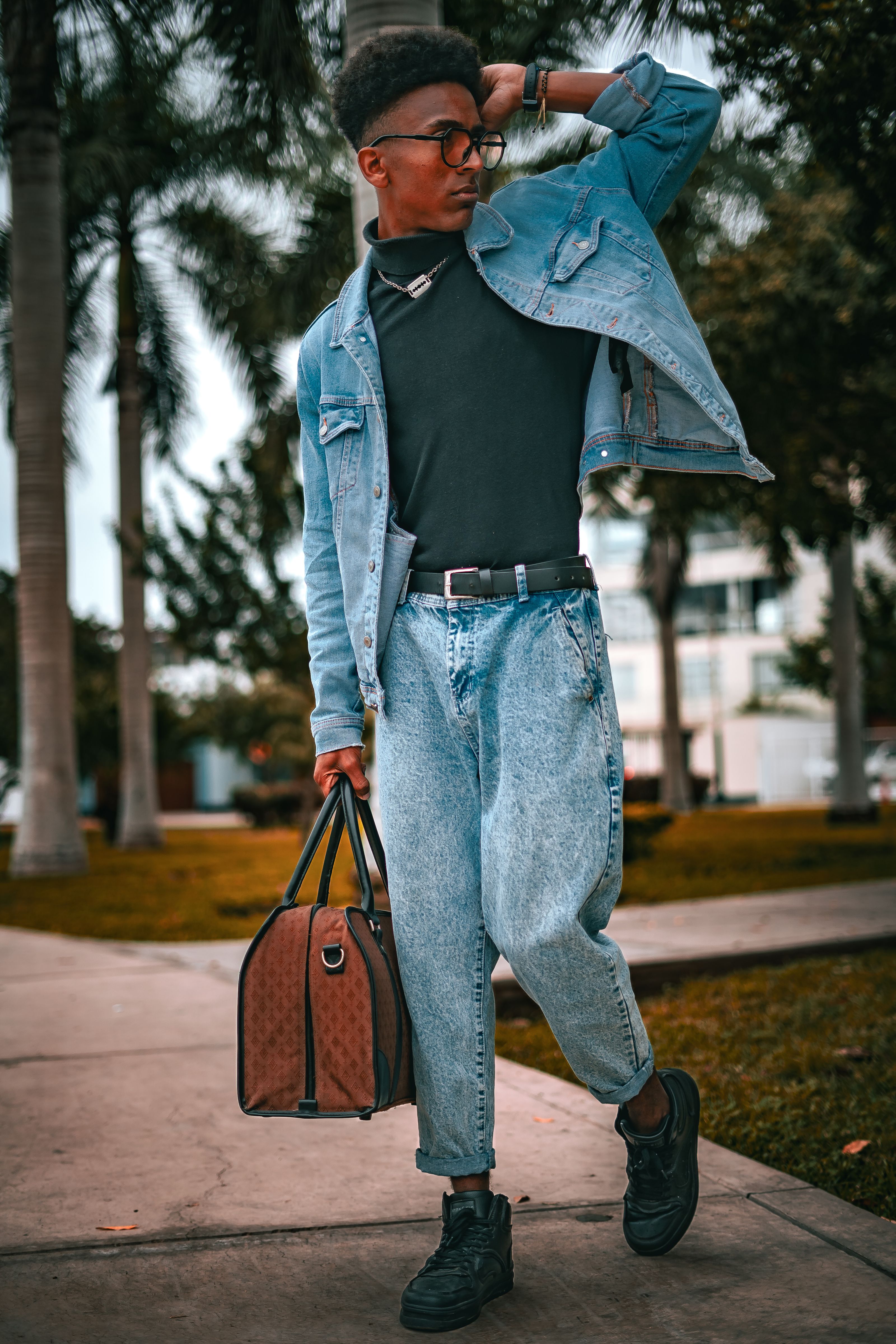 Homem fashionável de jeans com óculos de sol carregando uma bolsa ao ar livre.
