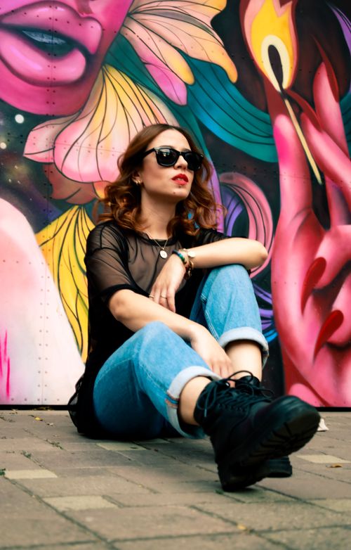Free Woman in jeans and boots sitting by a vibrant graffiti wall outdoors. Stock Photo