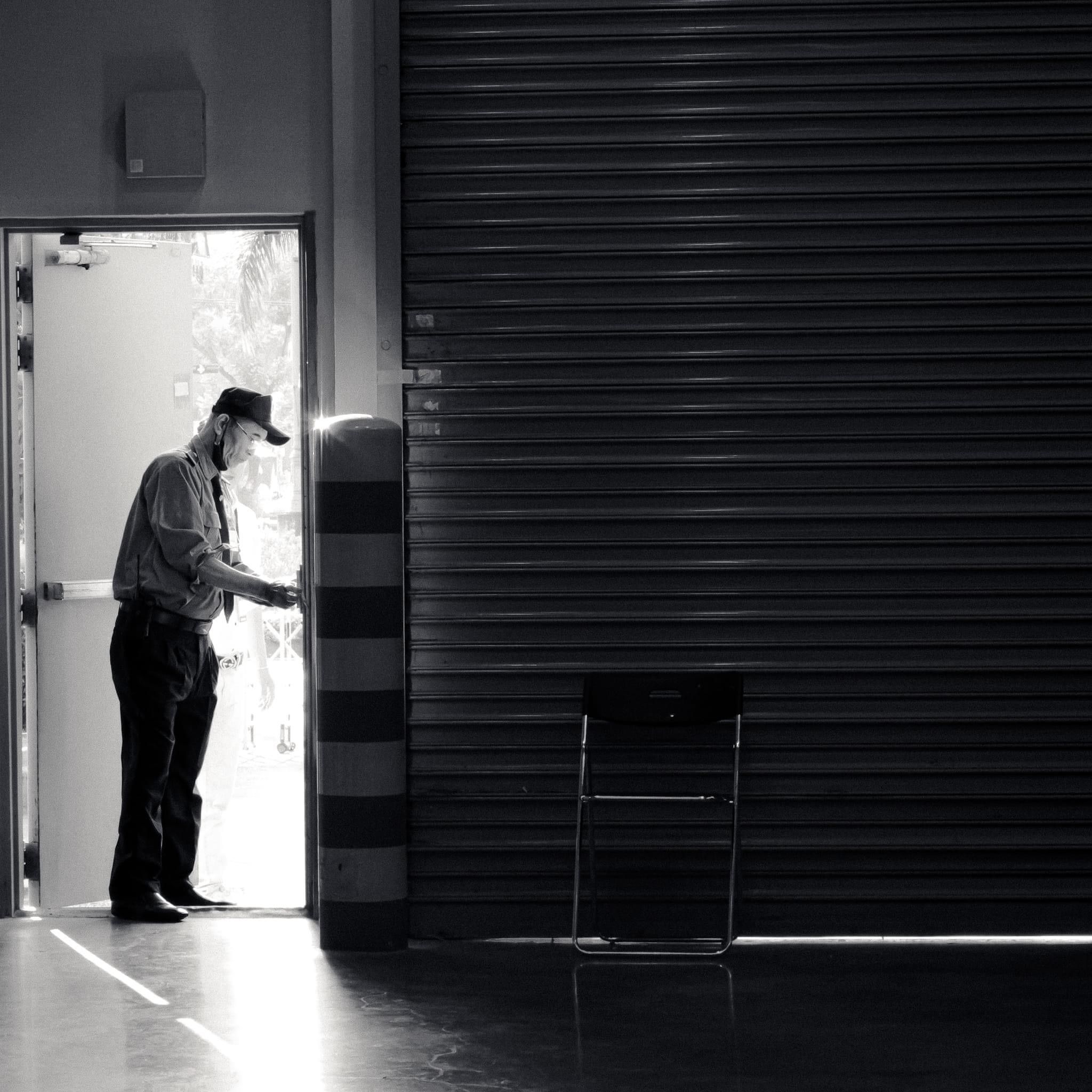 A black and white image of a security guard standing at an open industrial doorway.
