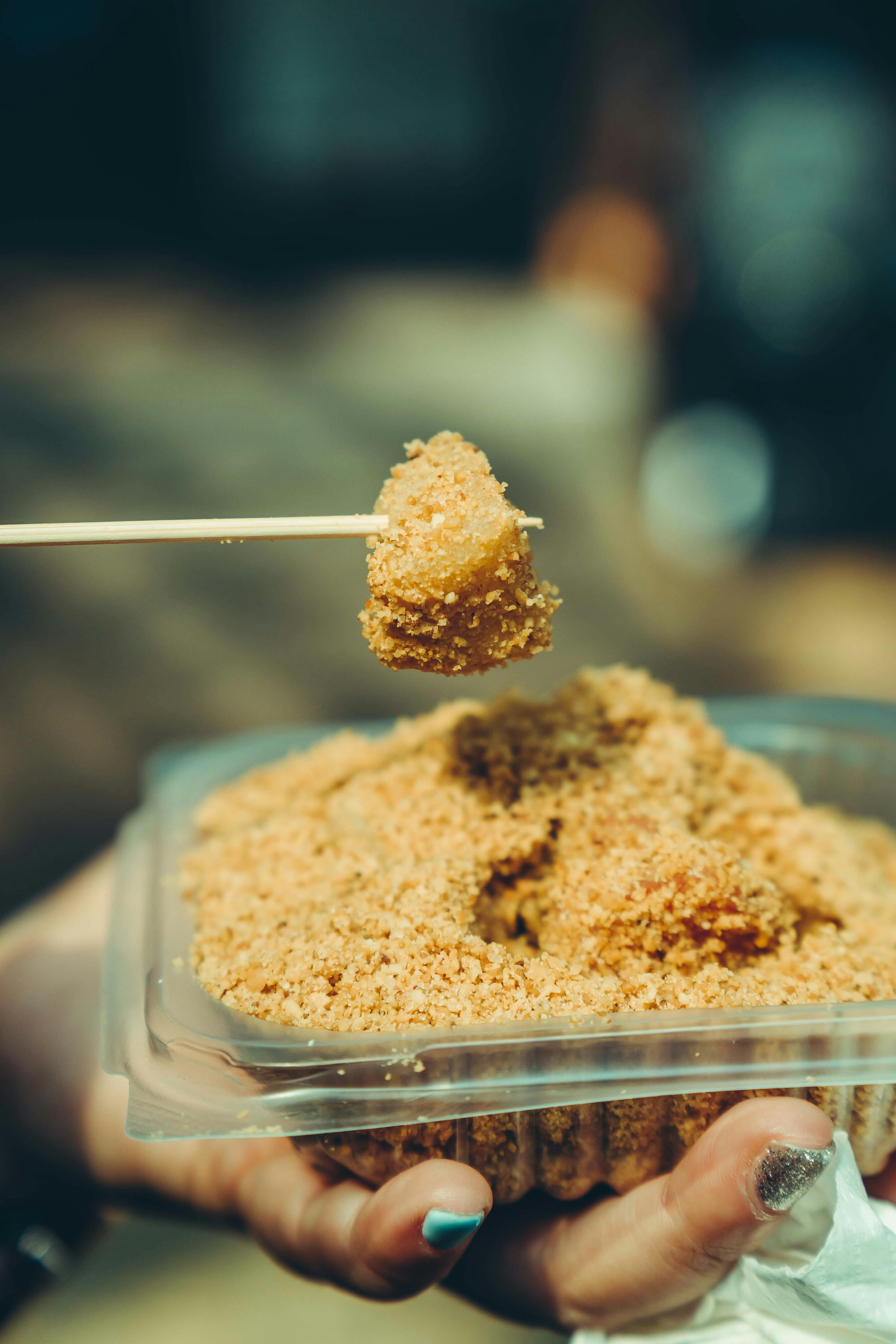 Close-up of a person holding Asian street food skewer over plastic container.