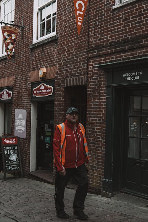 A man in an orange jacket standing in front of a brick building