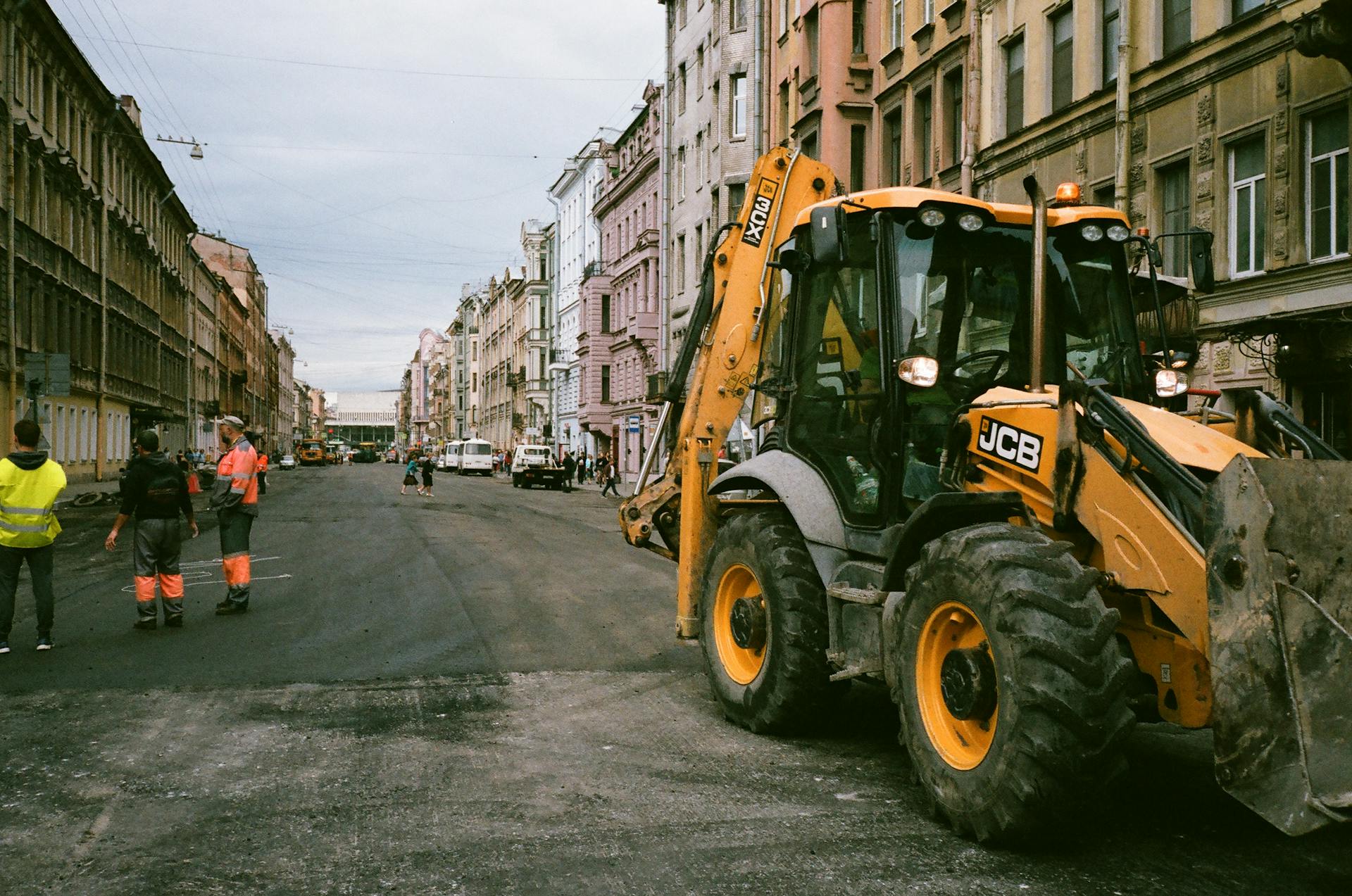 City street construction scene with workers and JCB excavator.