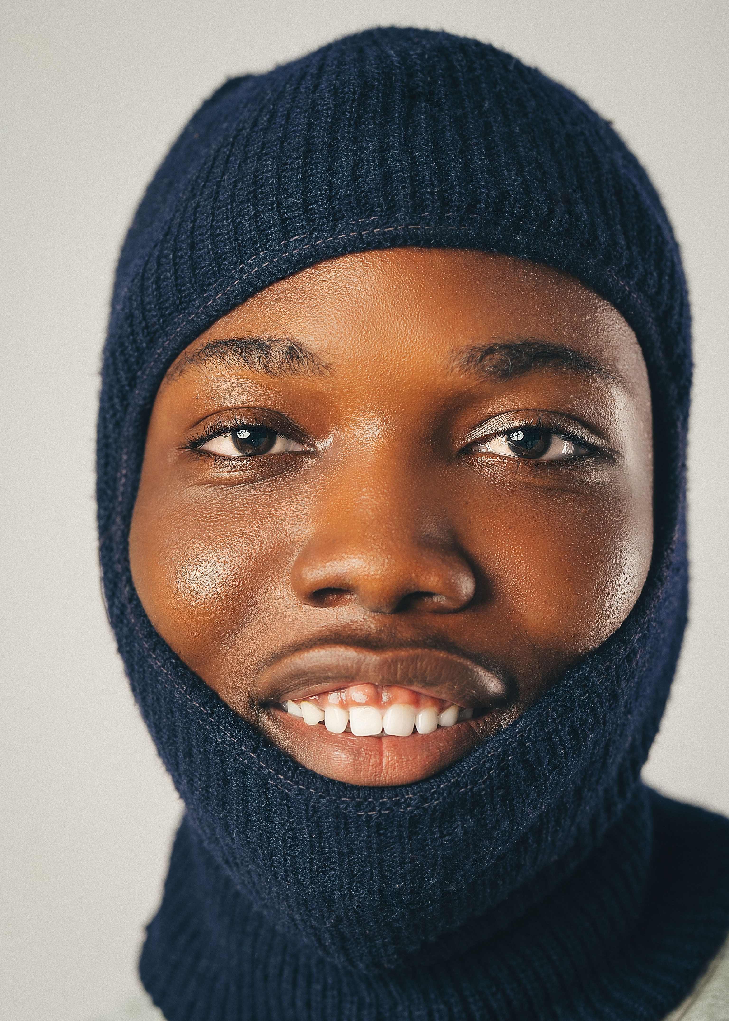Portrait of a young man in a navy balaclava, smiling warmly.