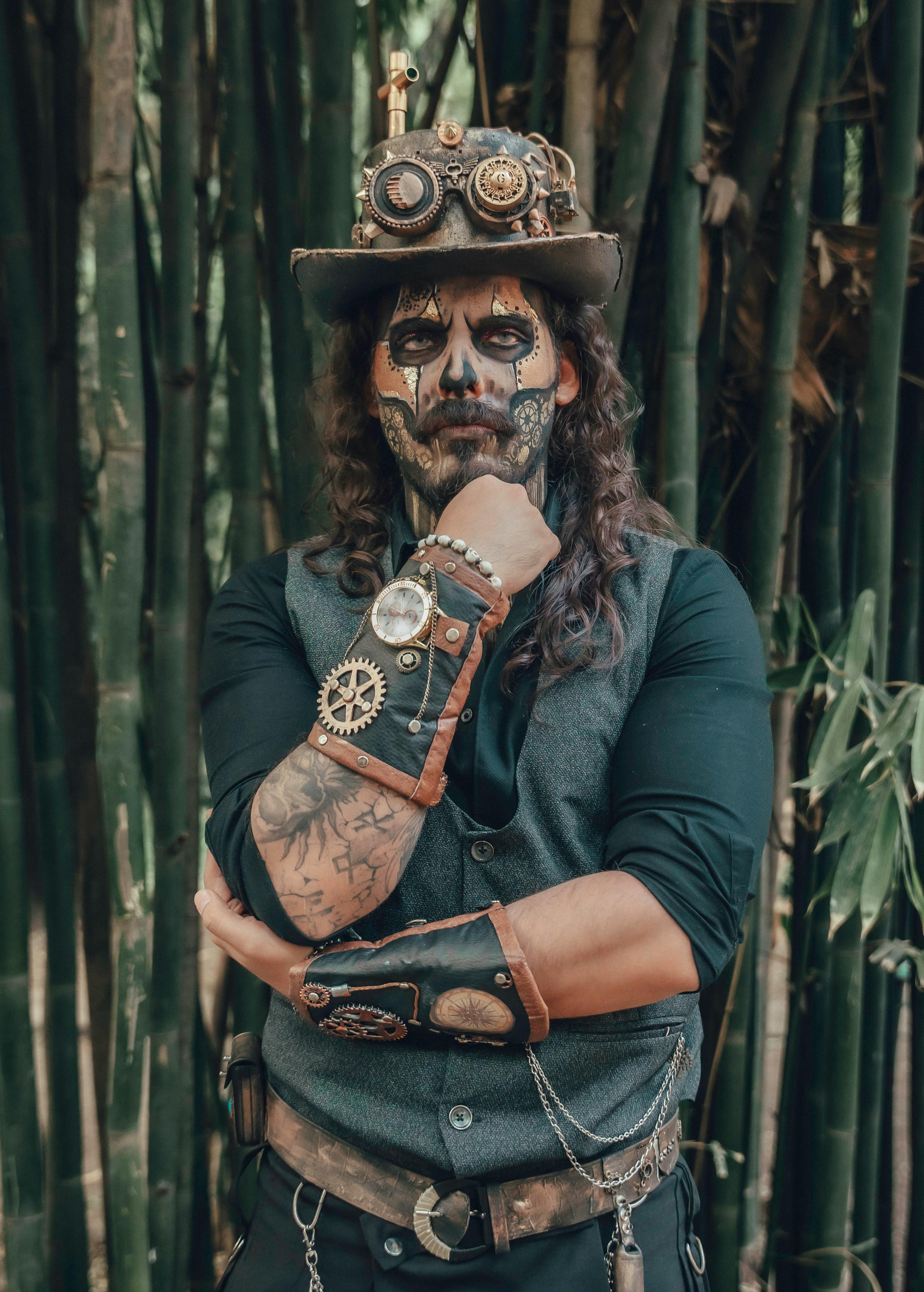 Portrait of a man in a detailed steampunk outfit with face paint, posing in a bamboo forest.