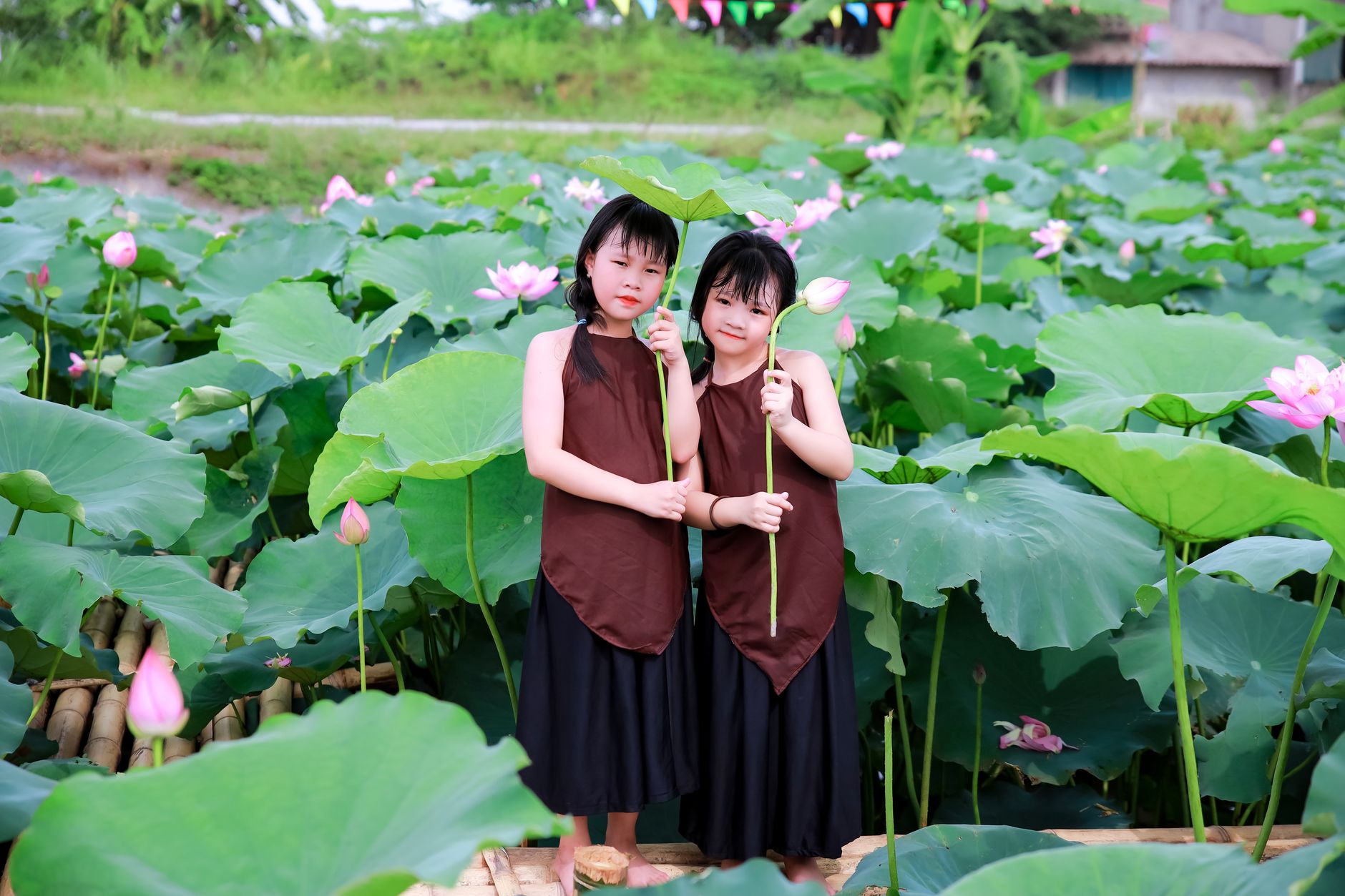 Two children holding lotus flowers in a lush garden. Vibrant and serene setting.
