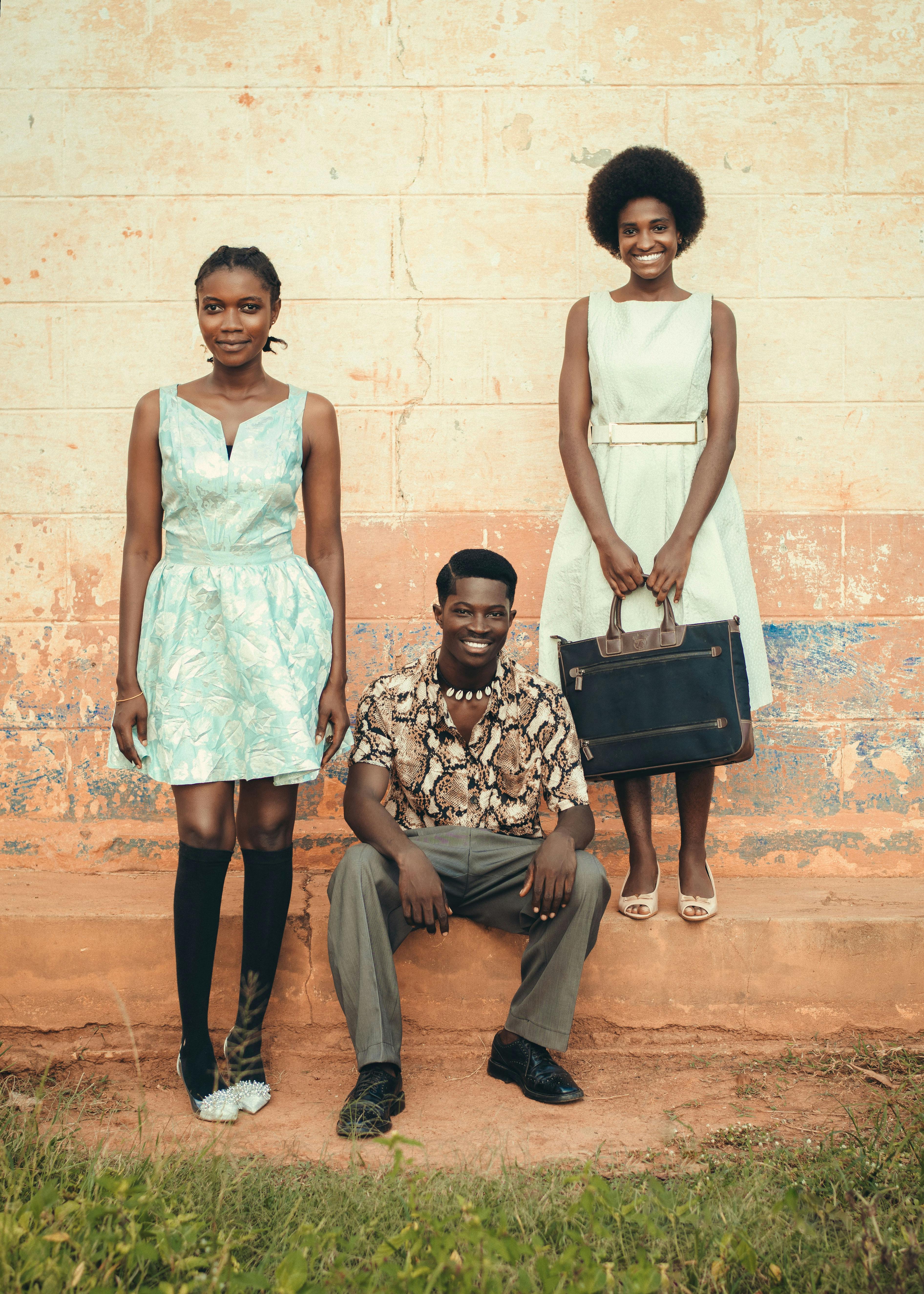 Trendy young adults in vintage attire pose stylishly against a rustic wall, showcasing retro fashion.
