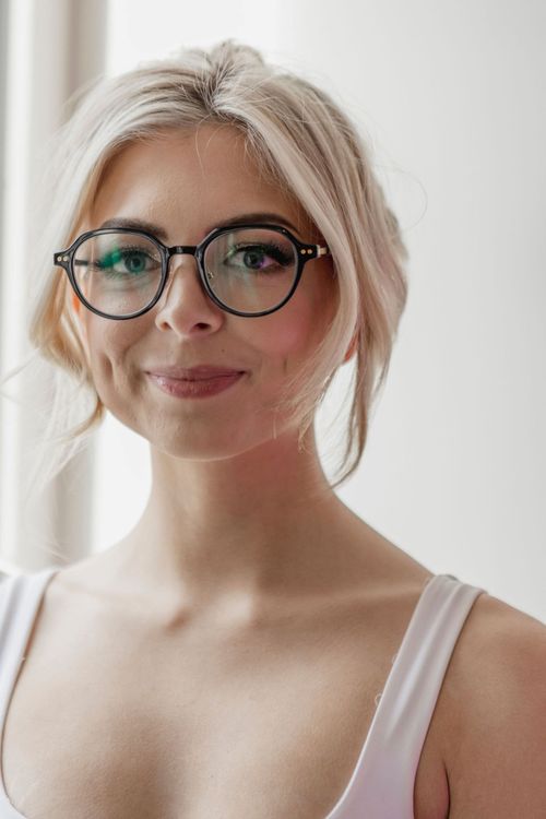 Free Close-up portrait of a young woman wearing fashionable glasses in a bright indoor setting. Stock Photo