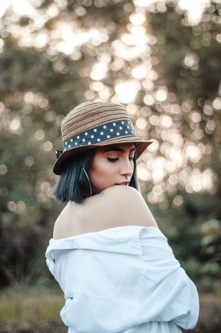 A stylish woman poses outdoors in a hat and off-shoulder outfit, highlighted by soft bokeh.
