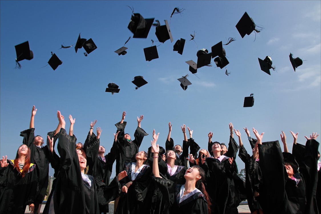 Newly Graduated People Wearing Black Academy Gowns Throwing Hats Up In