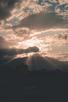 Captivating sunrise behind mountains with striking silhouette and sunbeams piercing clouds.