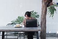 Woman Sitting at Table with Food and Laptop and Working