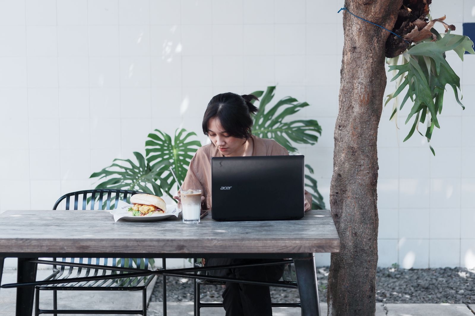 Woman working at a table with food and a laptop.