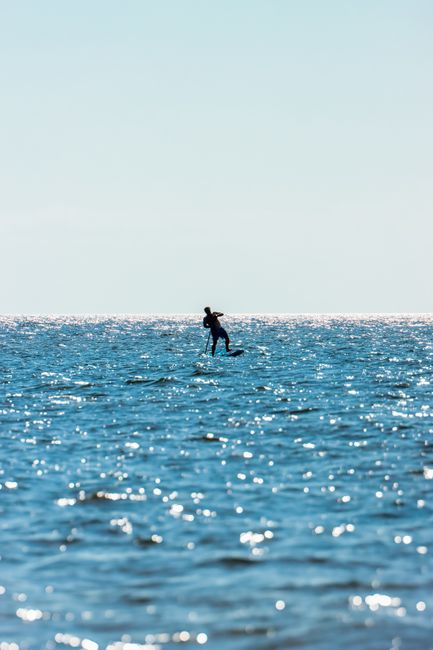 Silhouette of a person windsurfing on the sparkling blue waters of the Baltic Sea during a sunny summer day.