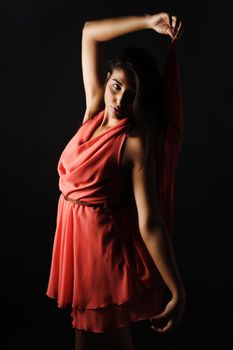 Stylish portrait of a young woman in a red dress against a dark studio background, fashion photography.