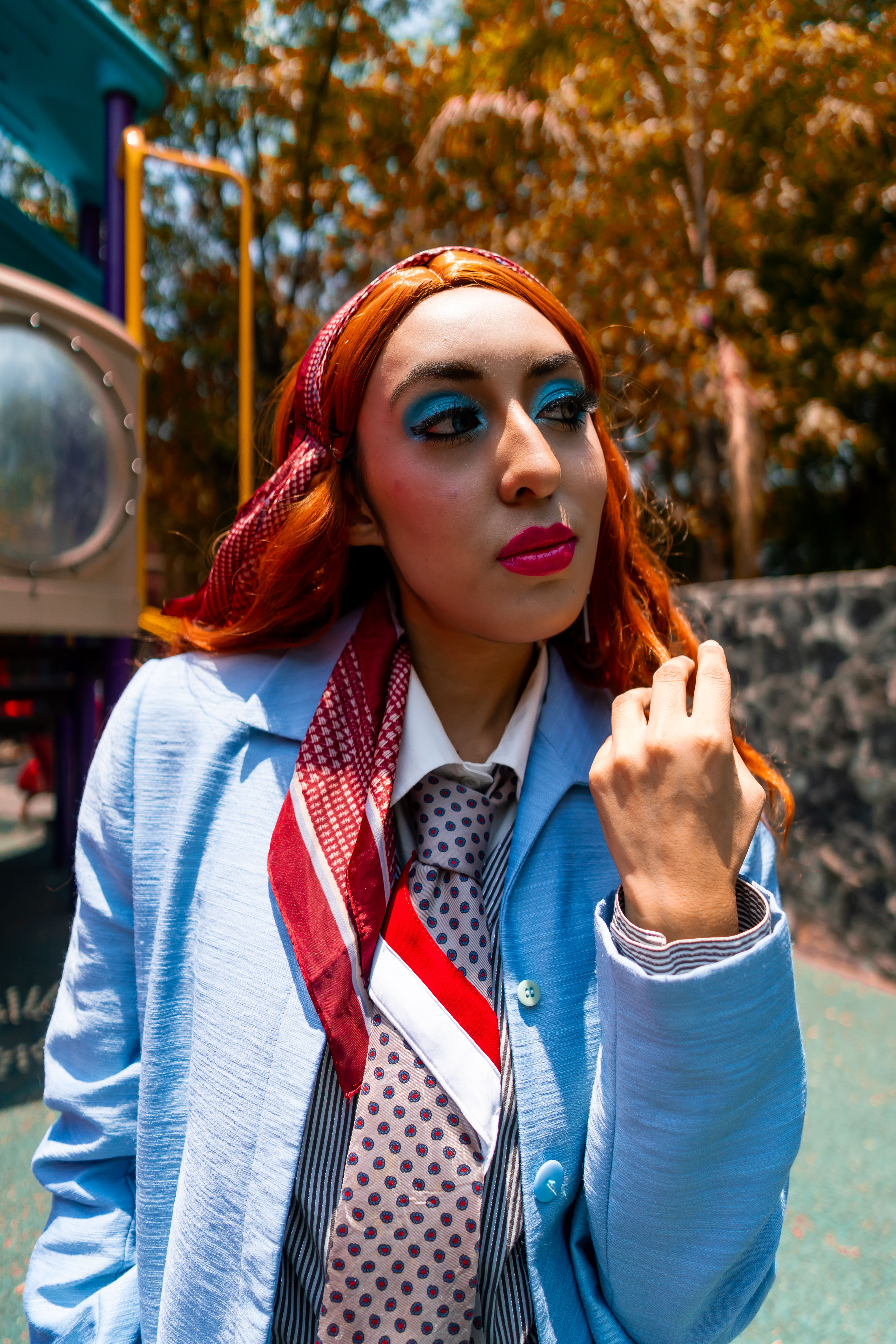 Fotomural Mujer elegante con maquillaje audaz y atuendo colorido en un entorno exterior soleado.
