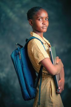 Portrait of a young student holding books and wearing a backpack against a studio backdrop.