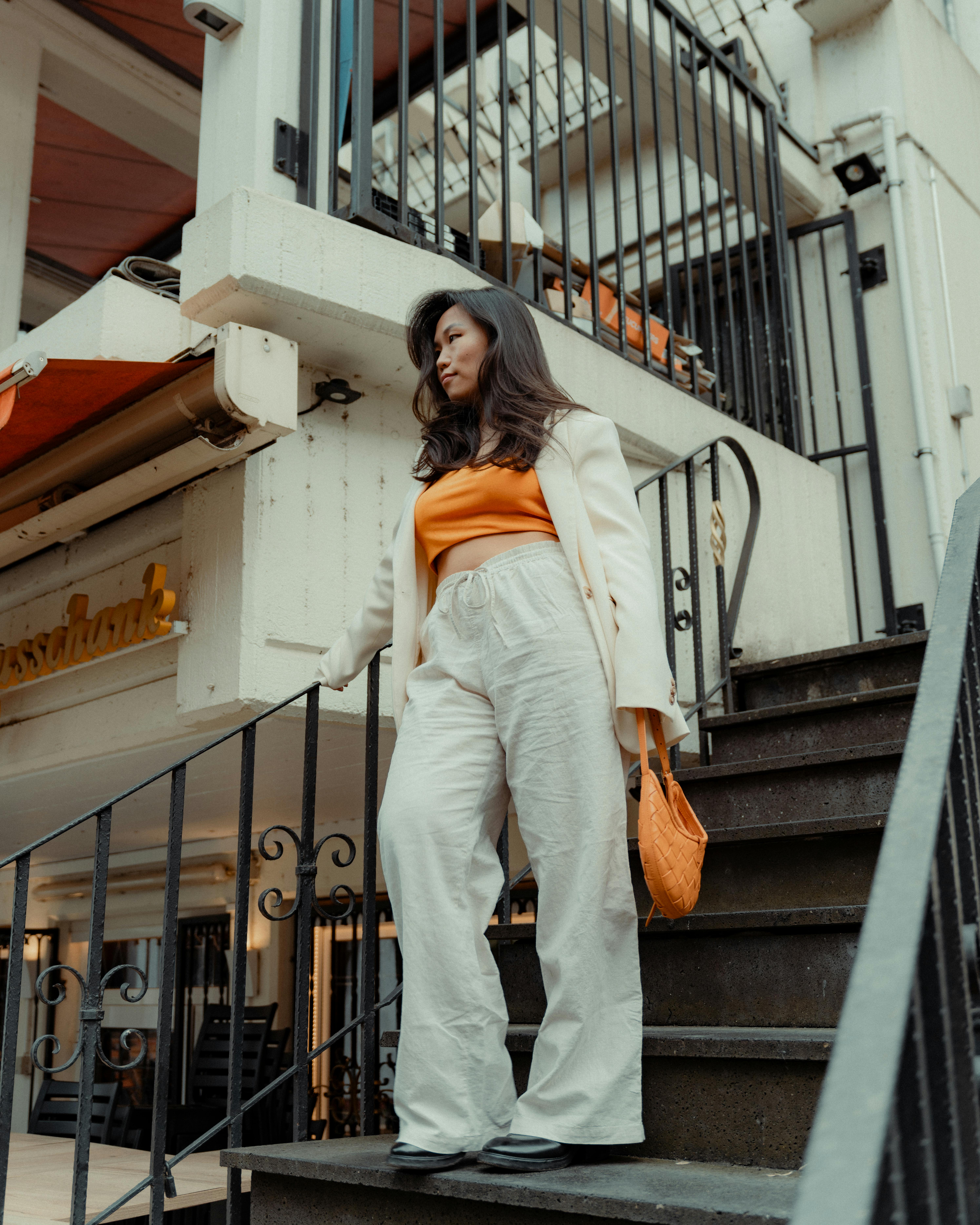 Confident woman in white suit with orange top walking down outdoor stairs in an urban setting.