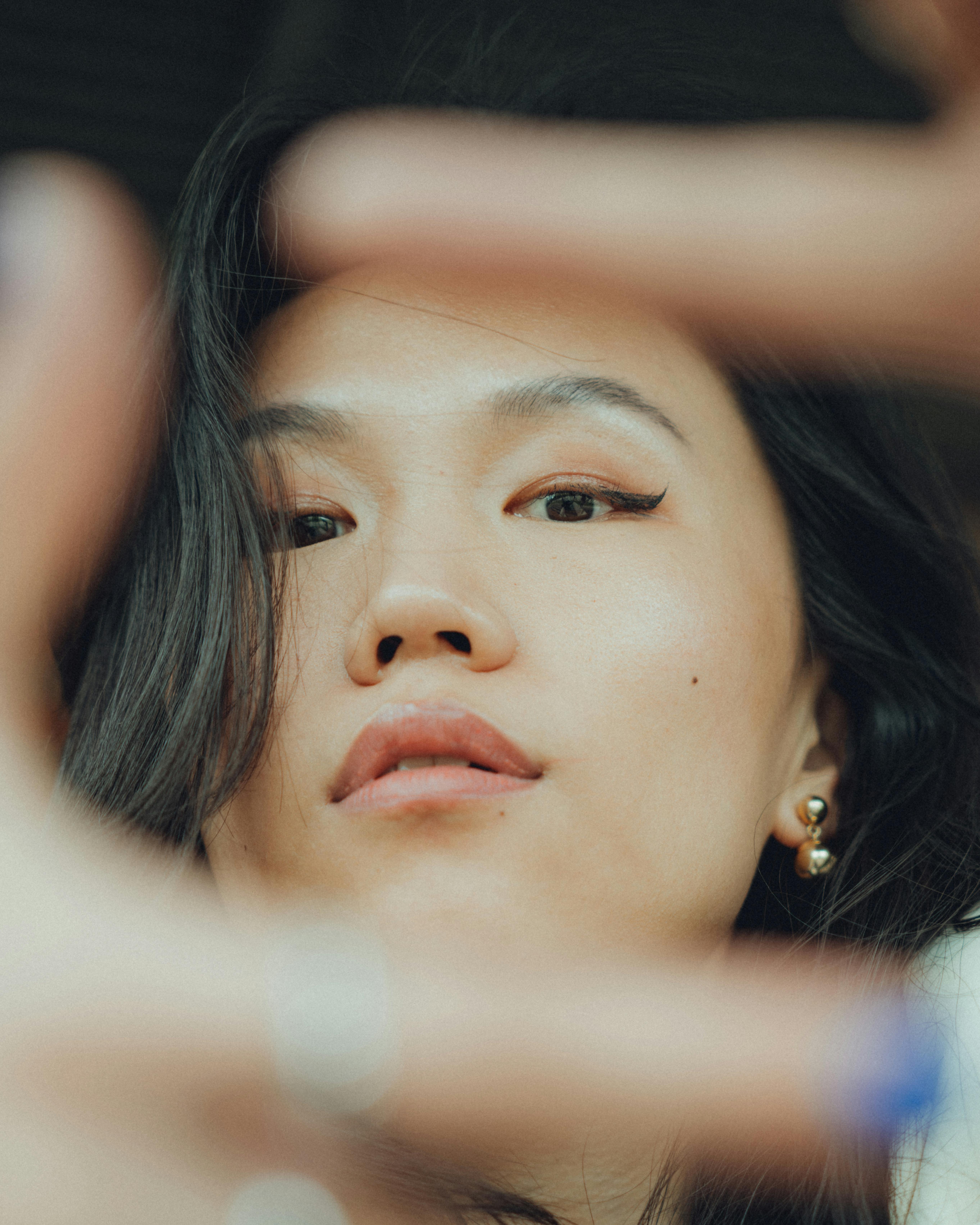 Close-up portrait of a young woman framed by fingers, showcasing a serious expression and selective focus.