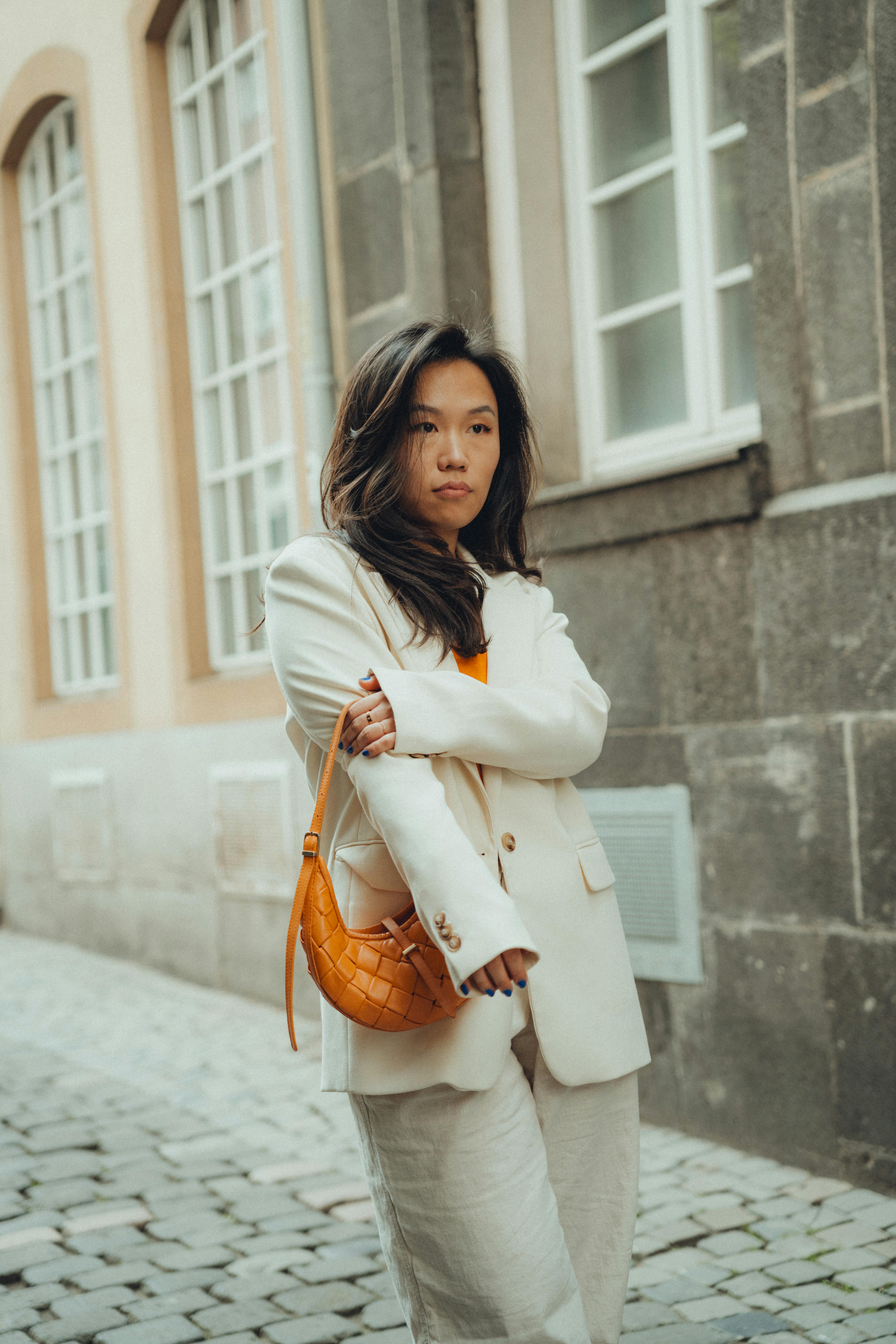 Stylish woman in a white suit poses on a charming city street.