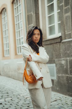 Stylish woman in a white suit poses on a charming city street.
