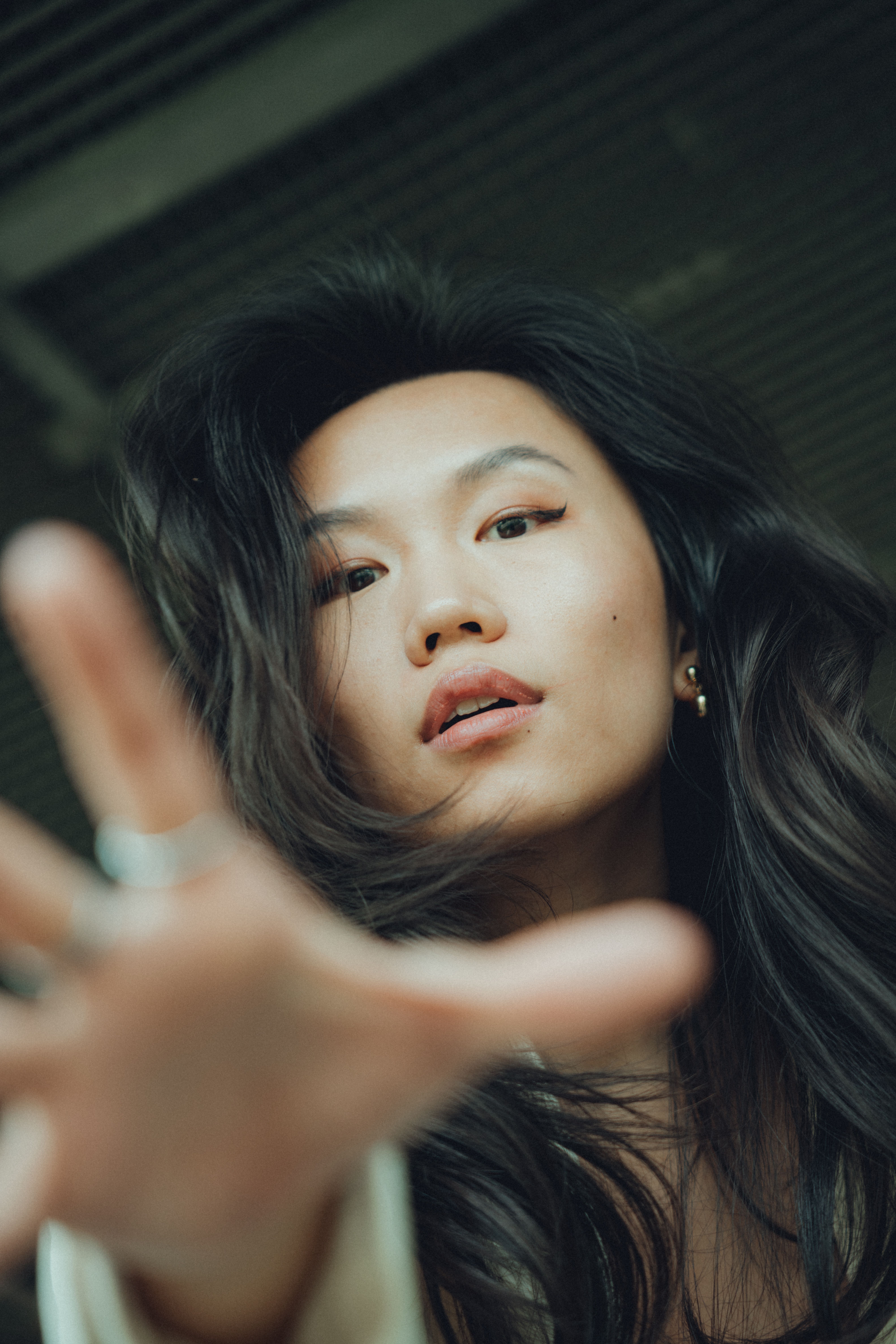 Artistic portrait of an Asian woman with long hair and a reaching gesture.