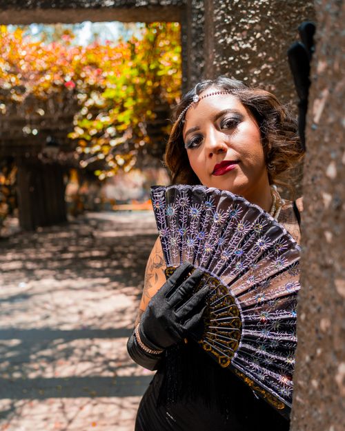 Free Stylish woman in black dress with hand fan in sunny Ciudad de México park. Stock Photo